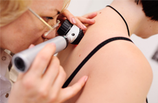 [Translate to Spanish:] Physician looking on skin of patient with an miscroscope instrument